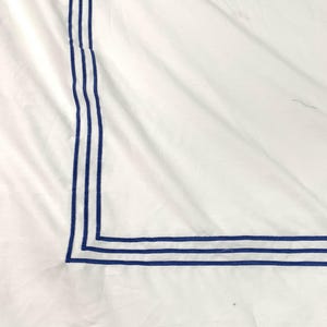 Pode incluir: Roupa de cama branca com uma borda azul ao redor da borda. A borda &eacute; feita de tr&ecirc;s linhas paralelas.