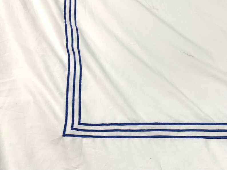 Pode incluir: Roupa de cama branca com uma borda azul ao redor da borda. A borda &eacute; feita de tr&ecirc;s linhas paralelas.