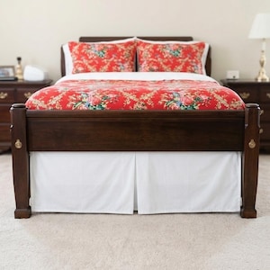 May include: A dark wood bed frame with a red floral patterned duvet cover and pillowcases. The bed has a white valance. The room has a neutral colour palette with a lamp and bedside tables on either side of the bed.