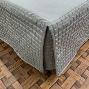 Może przedstawiać: Szara pikowana spódnica do łóżka z falbanką. Spódnica wykonana jest z miękkiej, wygodnej tkaniny i ma subtelny połysk.