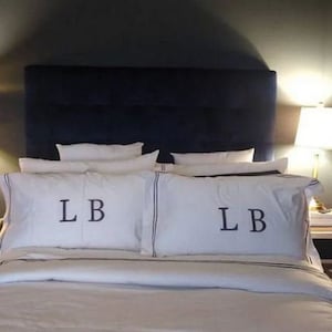 May include: A white bed with a navy blue headboard and white bedding. The pillows have the initials "LB" embroidered on them.