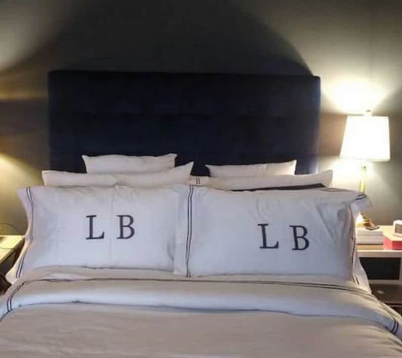May include: A white bed with a navy blue headboard and white bedding. The pillows have the initials "LB" embroidered on them.