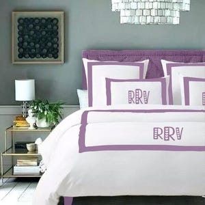 May include: White bedding with a purple border and the initials "RRV" embroidered on the pillow and duvet cover.