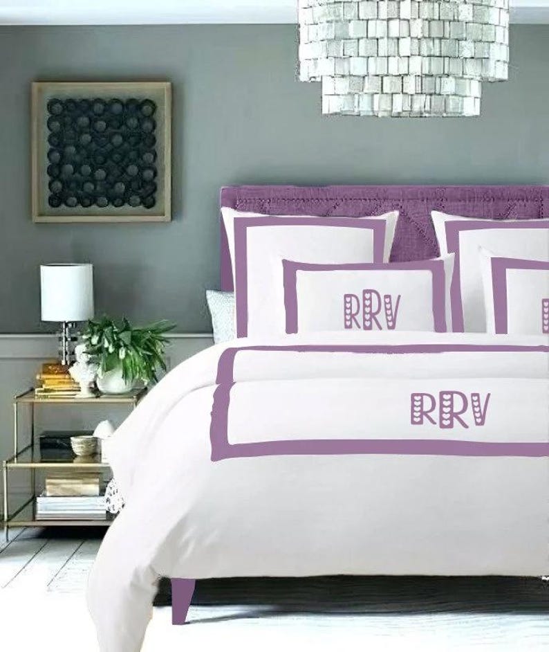 May include: White bedding with a purple border and the initials "RRV" embroidered on the pillow and duvet cover.