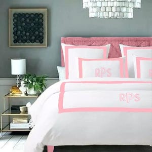 May include: White bedding with a pink border and the initials "RPS" embroidered on the pillow and duvet cover.
