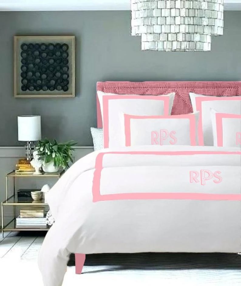 May include: White bedding with a pink border and the initials "RPS" embroidered on the pillow and duvet cover.