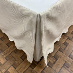 Può includere: Una gonna da letto beige con strisce bianche. La gonna è plissettata e ha un bordo a festoni.
