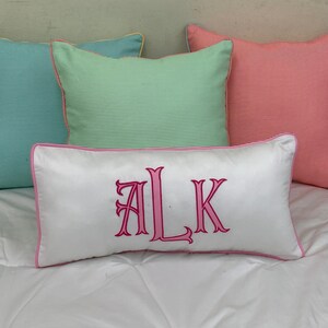 May include: Four decorative throw pillows in various colors. Three square pillows feature striped patterns in teal, green, and coral. The rectangular pillow is white with pink embroidered initials and a pink border.