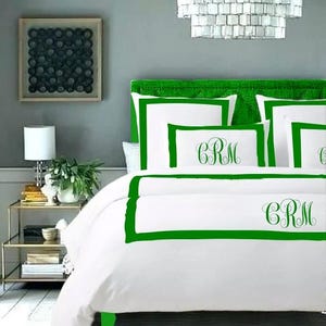 May include: White bedding with a green border and the monogram "CRM" embroidered on the pillow and duvet cover.