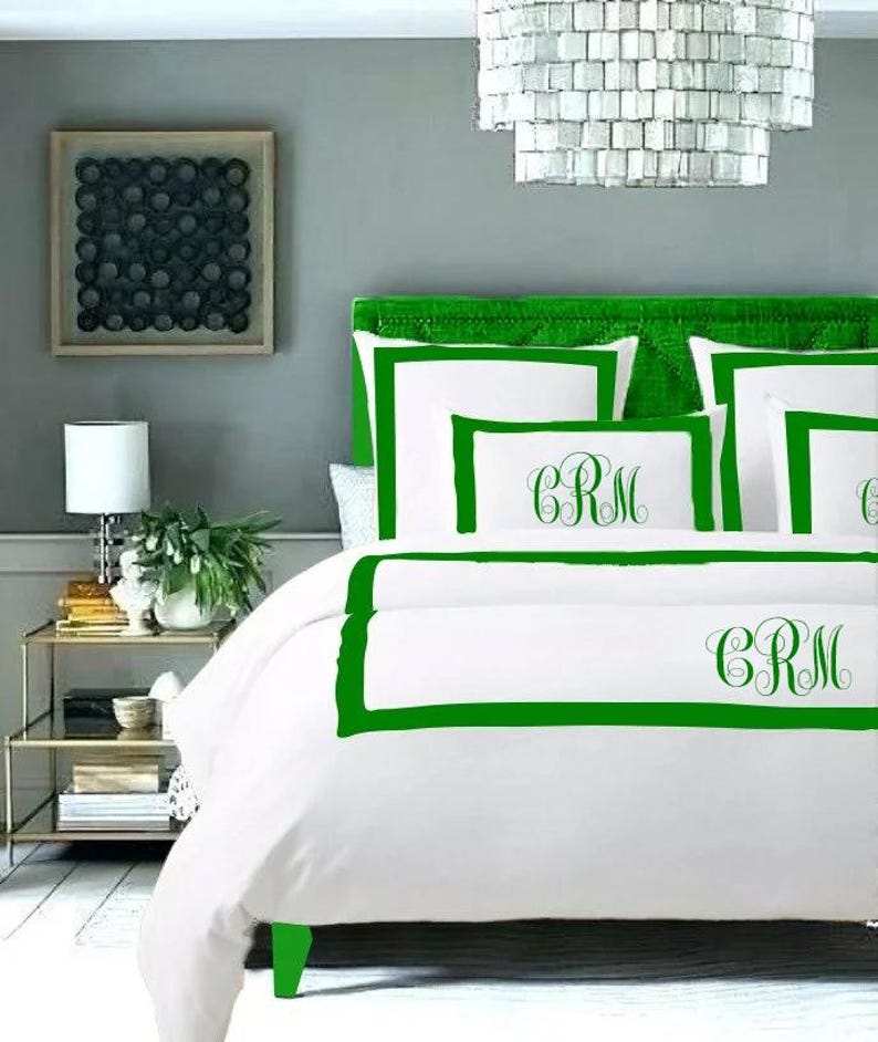 May include: White bedding with a green border and the monogram "CRM" embroidered on the pillow and duvet cover.
