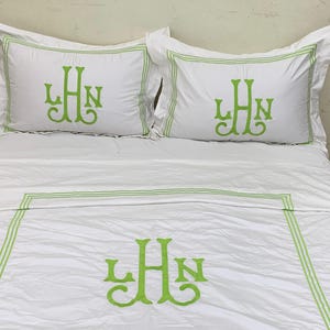 Puede incluir: Juego de cama blanco con monograma bordado en verde. El juego incluye dos fundas de almohada y una funda n&oacute;rdica, todas con un monograma estilizado en color verde vibrante. Las fundas de almohada y la funda n&oacute;rdica tienen un borde verde.
