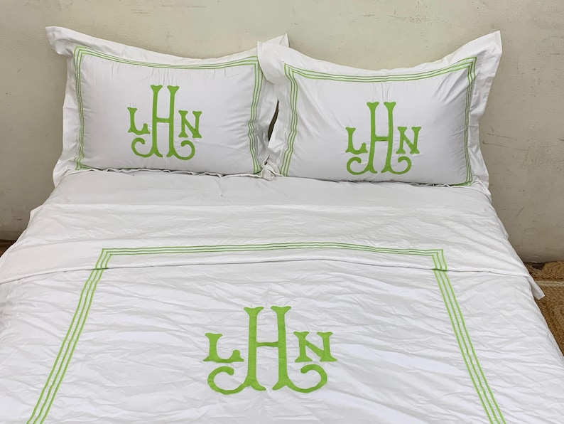 Puede incluir: Juego de cama blanco con monograma bordado en verde. El juego incluye dos fundas de almohada y una funda n&oacute;rdica, todas con un monograma estilizado en color verde vibrante. Las fundas de almohada y la funda n&oacute;rdica tienen un borde verde.
