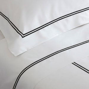 May include: White bed linens with a black double-stitched border.
