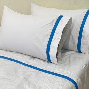 May include: White bedding set with blue accent stripes. The image shows two white pillowcases and a white duvet cover, all with a vibrant blue stripe detail. The bedding is neatly arranged on a bed, creating a clean and inviting look.