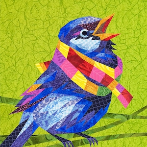 Op de afbeelding: Een blauwe vogel met een kleurrijke sjaal om zijn nek, gemaakt van patchwork stof. De vogel zingt met zijn bek open en heeft een felgroene achtergrond.