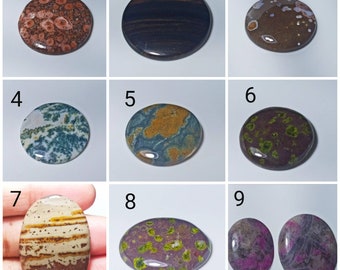 May include: A collection of nine polished gemstones in various shapes and colors. The stones include round and oval shapes, with colors ranging from brown, blue, green, and purple. Some stones have unique patterns and textures, perfect for jewelry making or collecting.