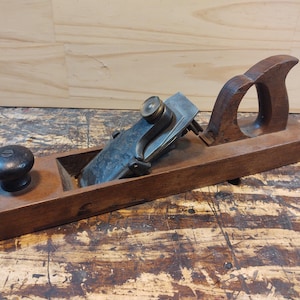 May include: A vintage wooden hand plane with a metal blade and a wooden handle. The plane is in good condition and has a dark brown finish.