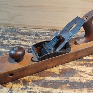 May include: A vintage wooden hand plane with a metal blade and a wooden handle. The plane is in good condition and has a dark brown finish.