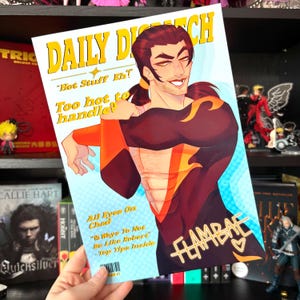 May include: A print featuring a stylized illustration of a man on a magazine cover. The magazine title reads "DAILY DISPATCH" in yellow. Text includes "Hot Stuff Eh?" and "Too hot to handle!" The illustration is in shades of red, orange, and black. The word "FLAMBAE" is also visible.