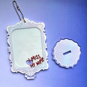 May include: A rectangular acrylic frame with an ornate, light-colored border and a silver ball chain, featuring the red text "I MISS MY WIFE" and a small heart cutout. Beside it is a circular acrylic base with a slot for the frame to stand upright.