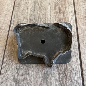 May include: A vintage metal cookie cutter shaped like a sheep. The cutter is dark gray with a worn, rustic look. It has a small hole in the center for hanging.
