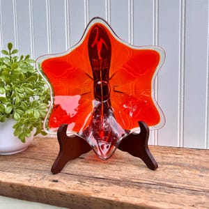 May include: A star-shaped glass dish with a red and orange color gradient. The dish is on a wooden stand.