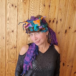 Puede incluir: Una mujer con un top negro y una diadema de fieltro morado, azul y naranja. La diadema tiene un diseño caprichoso y abstracto.