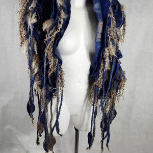 Op de afbeelding: Een blauwe en bruine wollen sjaal met lange franjes. De sjaal is over een wit mannequin gehangen.