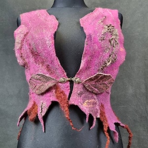 May include: A pink sleeveless vest with brown felt leaf accents and a metal clasp closure. The vest has a frayed, distressed look and is made of felted wool.