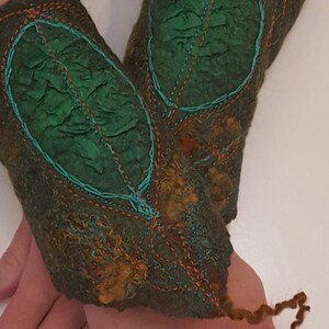 Può includere: Un paio di scaldamani in feltro verde e marrone con cuciture turchesi e motivi a foglia.