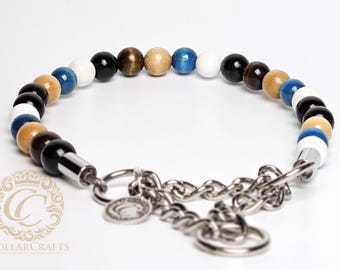 May include: A beaded collar featuring a repeating pattern of smooth, round beads in shades of blue, white, black, and tan. The collar includes a silver-toned metal chain section with a circular ring and a small circular charm with the text COLLARCRAFTS.