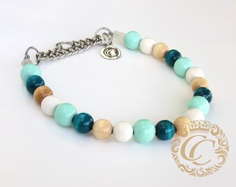 May include: A teal, white, and beige wooden bead necklace with a silver chain clasp. The necklace is made of round beads and has a silver charm with a logo.