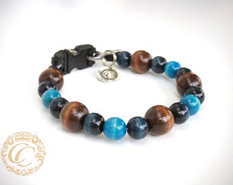 May include: A beaded bracelet featuring alternating brown, blue, and turquoise-colored beads. The bracelet has a black clasp and a silver charm. The beads are round and appear to be made of stone or wood.
