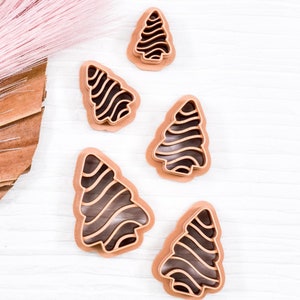 May include: Five brown plastic cookie cutters shaped like Christmas trees with a wavy line design.