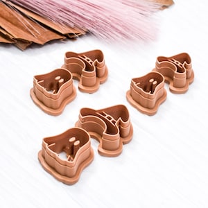 May include: Five brown plastic cookie cutters shaped like ghosts. The cutters are arranged in a row on a white surface.