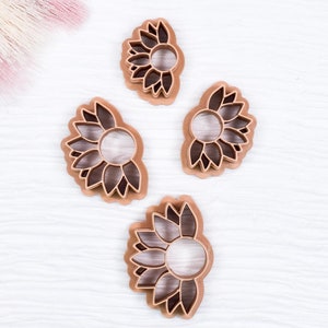 May include: Four brown metal cookie cutters shaped like sunflowers of different sizes.