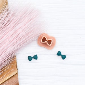May include: A flat lay featuring a pink feather boa, a brown and tan fan-shaped object, and three small bow-shaped objects. Two of the bows are teal blue and one is peach.