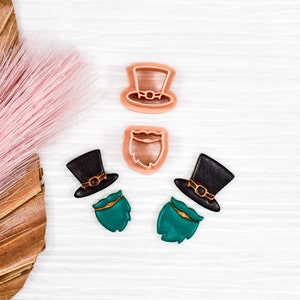 May include: Two green and black fondant toppers shaped like a leprechaun's hat and beard. Two plastic cookie cutters shaped like a leprechaun's hat and beard in pink.