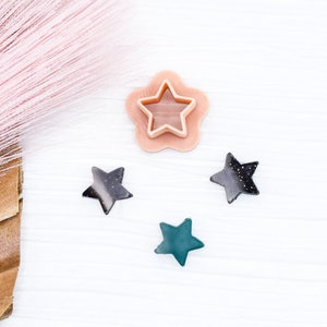 May include: Four star-shaped embellishments, two black, one green, and one peach. The peach star is a cookie cutter with a raised edge.