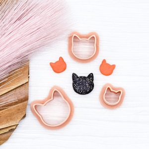 May include: A set of six cat-shaped cookie cutters, including two large, two small, and two medium-sized cutters. The cutters are made of pink plastic and are arranged on a white surface.