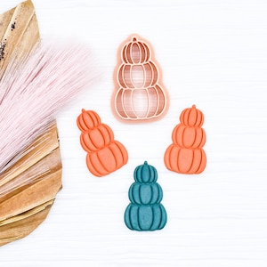 May include: Three stackable pumpkin cookie cutters, one in teal and two in orange. The teal cutter is a single pumpkin, while the orange cutters are stacked in a pyramid shape.