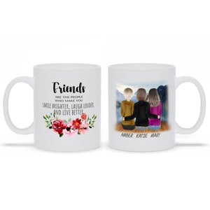 Puede incluir: Taza de cerámica blanca con la inscripción "Friends" y un diseño floral, junto con la cita "Are the people who make you smile brighter, laugh louder, and live better." El otro lado muestra tres figuras con los nombres Amber, Katie y Mary.