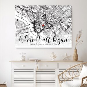 May include: A black and white city map print with a red dot marking a location. The text "Where it all began" is written in a cursive font below the map, with the names "Adam & Jessica" and the date "02.14.2020" written below the text.