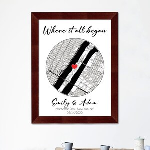 May include: A framed print with a black and white map of a city with a red heart marking a location. The text "Where it all began" is at the top of the print. Below the map, the text reads "Emily & Adam, Manhattan Park | New York, NY, 02/14/2020".