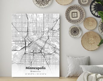 May include: A black and white map print of Minneapolis, Minnesota with the city's coordinates. The print is hanging on a white wall with a light brown wooden shelf below it. The shelf has a white throw blanket, a white pillow, and two woven baskets.