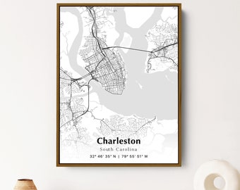 May include: A black and white map print of Charleston, South Carolina with the city's name and coordinates. The map is framed in a gold frame and is hanging on a white wall.