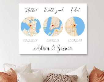 May include: A white canvas print with three maps of different cities, each with a red heart marking a location. The dates 03/12/2017, 15/08/2018, and 13/09/2019 are printed below each map. The text "Hello!" is above the first map, "Will you?" is above the second map, and "I do!" is above the third map. The text "Adam & Jessica" is printed below the maps.