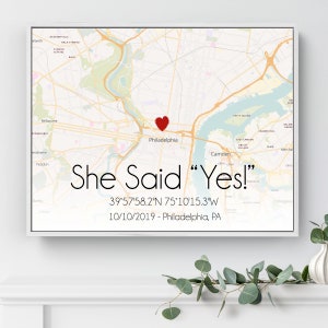 May include: A white framed map of Philadelphia, Pennsylvania with a red heart marking the location of the city. The text "She Said "Yes!" 39&deg;57'58.2"N 75&deg;10'15.3"W 10/10/2019 - Philadelphia, PA" is printed below the map.