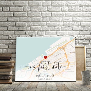 Puede incluir: Una impresi&oacute;n en lienzo con un mapa de Cleveland, Ohio, con un coraz&oacute;n rojo que marca la ubicaci&oacute;n de una primera cita. El texto "our first date" est&aacute; escrito en cursiva debajo del coraz&oacute;n. Los nombres "sophia & ronald" y la fecha "02-15-2019" est&aacute;n escritos debajo del texto.