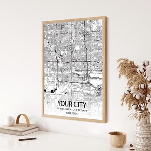 May include: A black and white city map print in a light wood frame. The map shows the streets and landmarks of a city. The text below the map reads "YOUR CITY", "33° 26′ 54.1536″N 112° 4′ 26.5296″W", and "YOUR STATE".